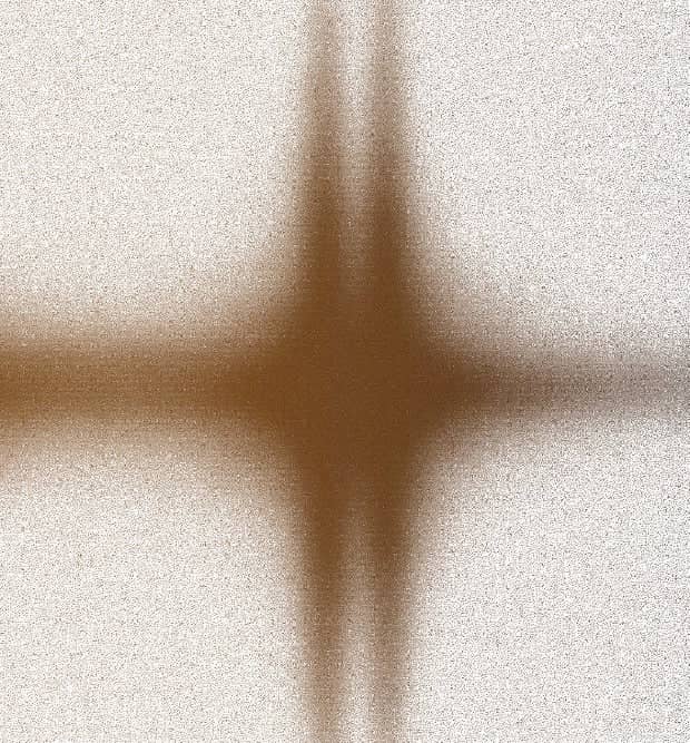 A soft, blurred cross-shaped shadow in warm brown tones against a textured off-white background.