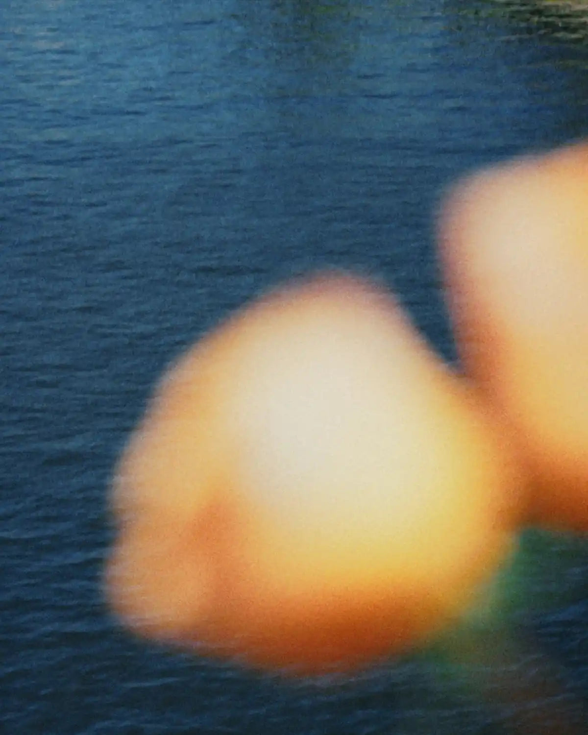 Two blurry, out-of-focus, light orange, rounded objects against a blue, rippled water background.